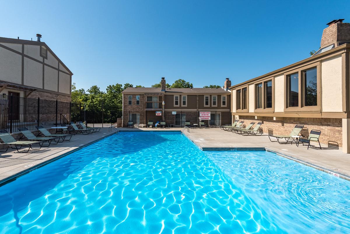 A large swimming pool in front of a building with lounge chairs around it.